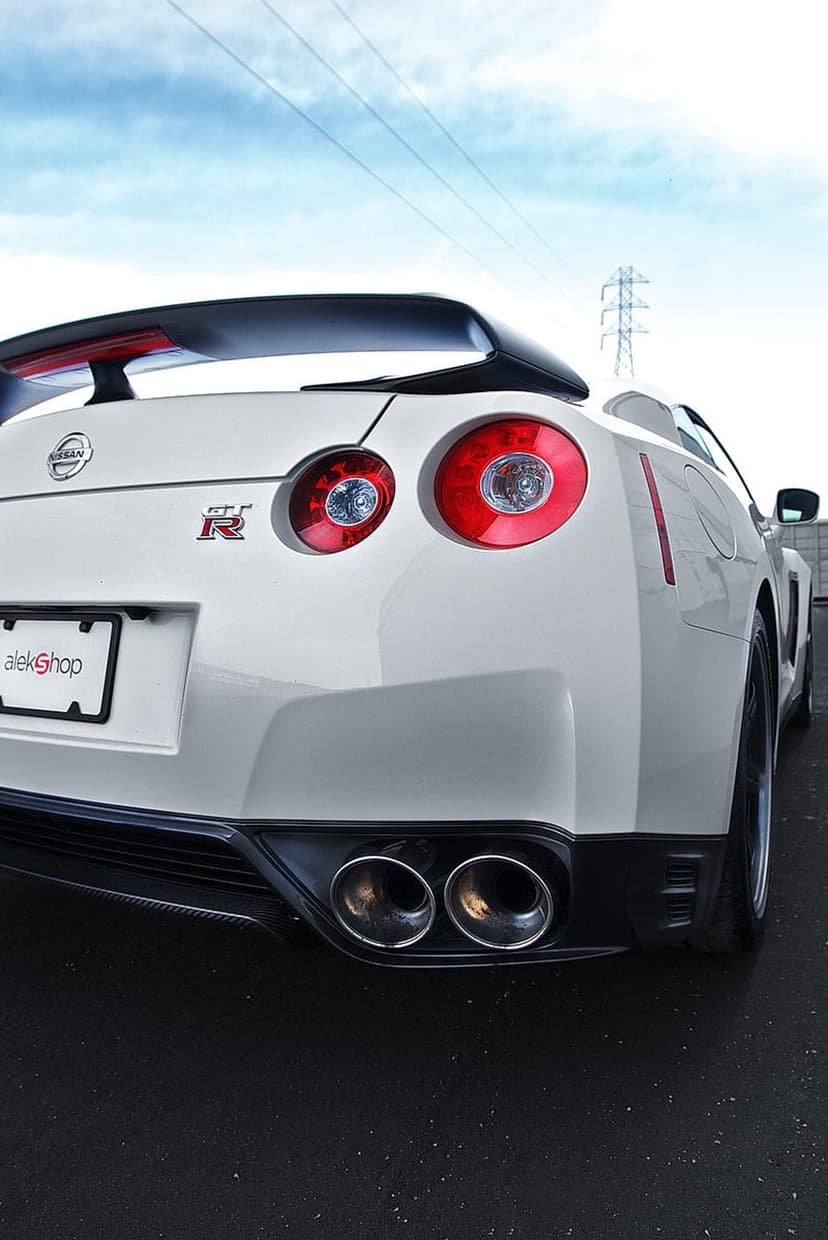 Nissan GT-R rear view featuring glowing red circular taillights, a large spoiler, and quad exhausts under a gray sky.
