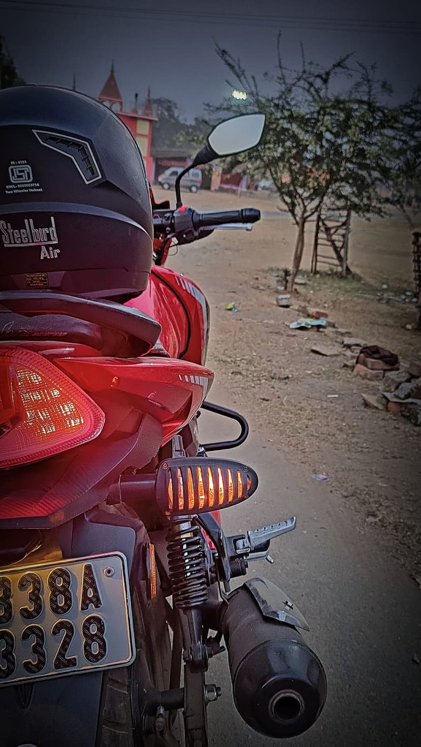 Red motorcycle rear view featuring a black helmet on the seat and glowing orange turn signals at twilight.