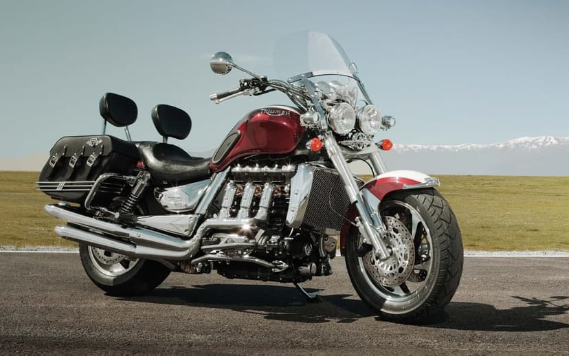 Red Triumph Rocket III motorcycle with chrome accents on a road with snowy mountains in the distance.