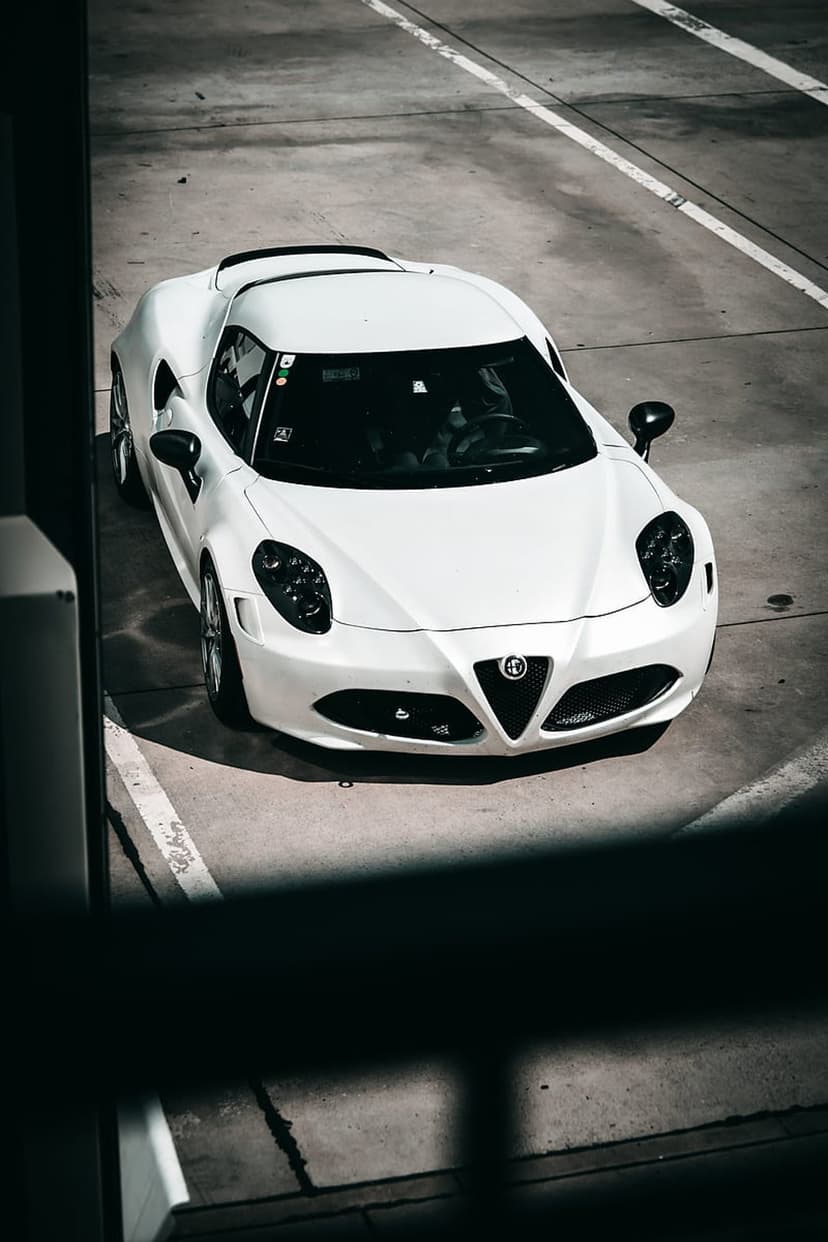 White Alfa Romeo 4C sports car parked on grey concrete with white lines seen from a direct overhead perspective.