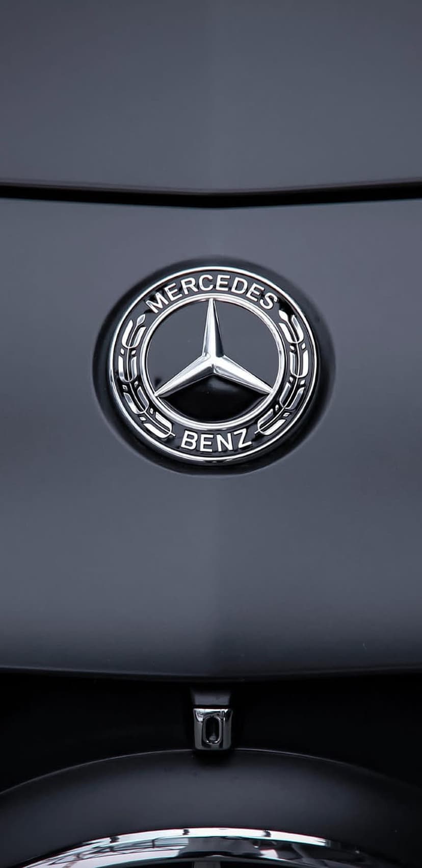 Silver Mercedes-Benz three-pointed star emblem mounted on a reflective black car hood with sharp chrome details.