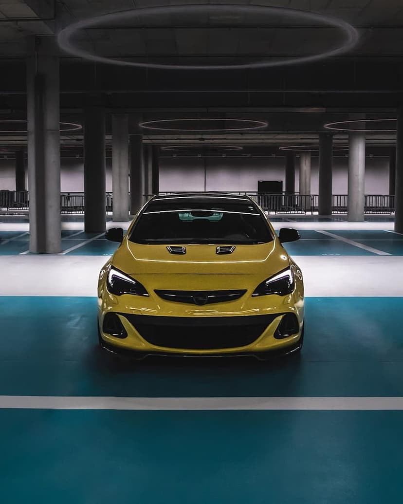 Yellow sports car parked on blue polished floors in a modern garage with circular overhead lights and pillars.