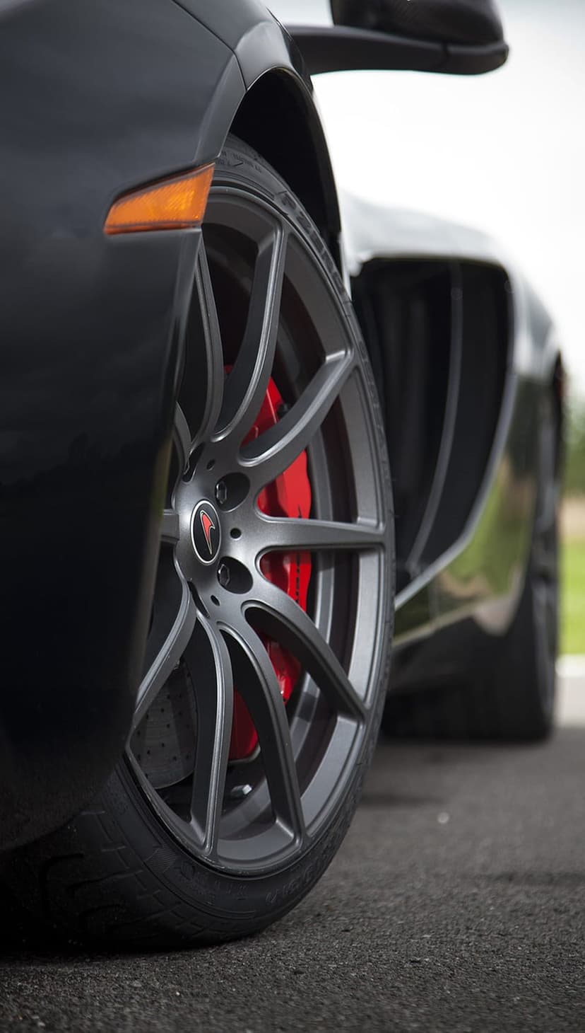 Matte grey multi-spoke wheel rim revealing bright red brake calipers on a dark performance car outdoors.