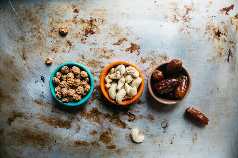 Turquoise, orange, and brown bowls containing tiger nuts, cashews, and dates on a textured, rustic surface.