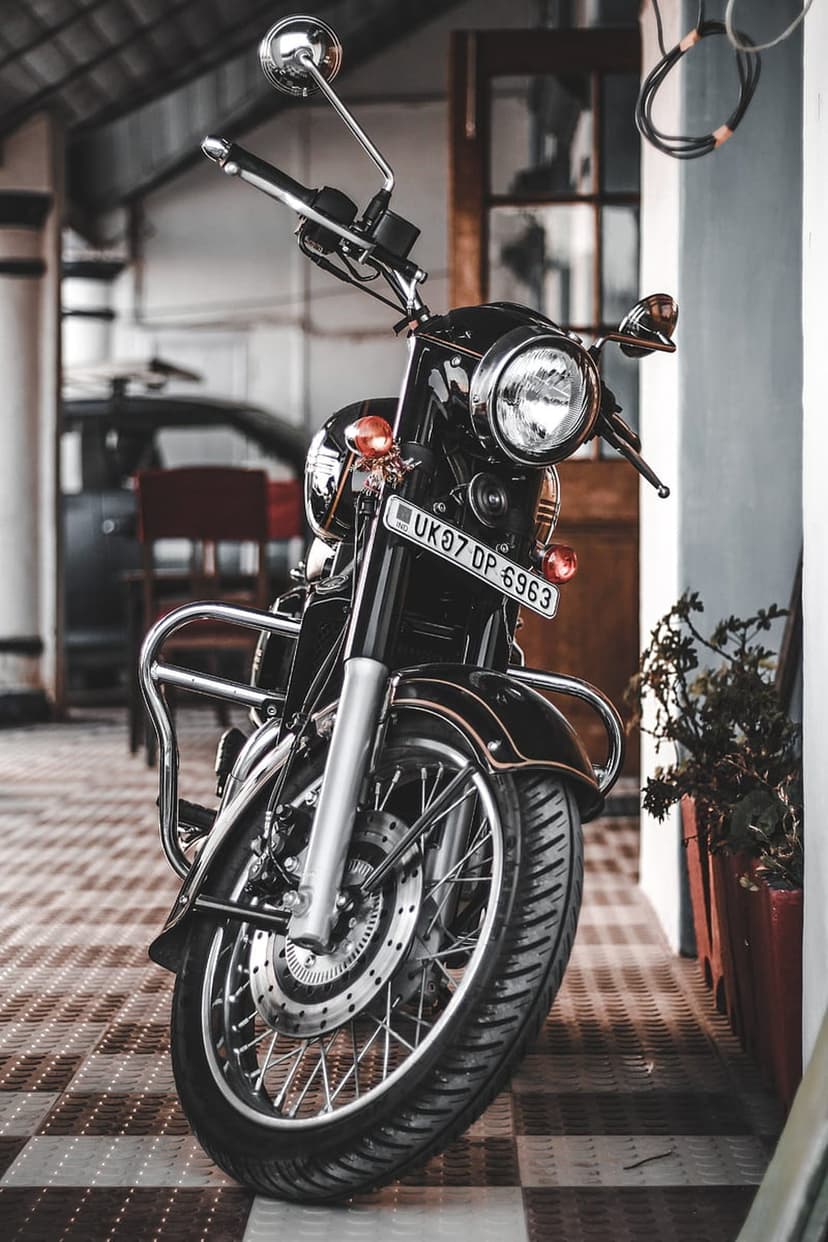 Classic black motorcycle featuring a round headlight and chrome accents parked on a white tiled floor indoors.