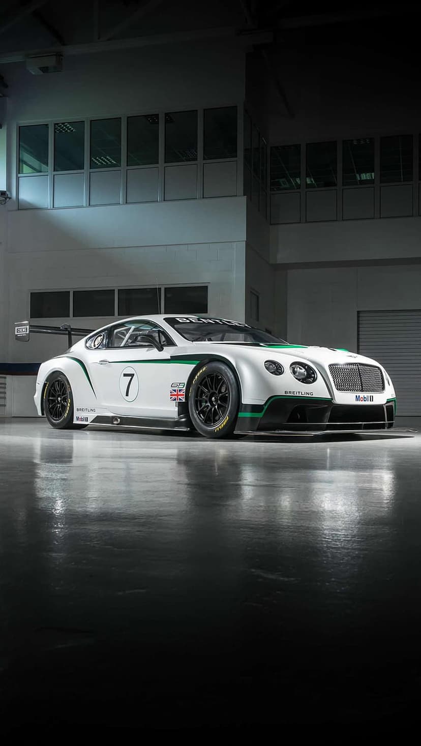Bentley Continental GT3 race car with white and green livery parked on a reflective floor in a bright pit lane.
