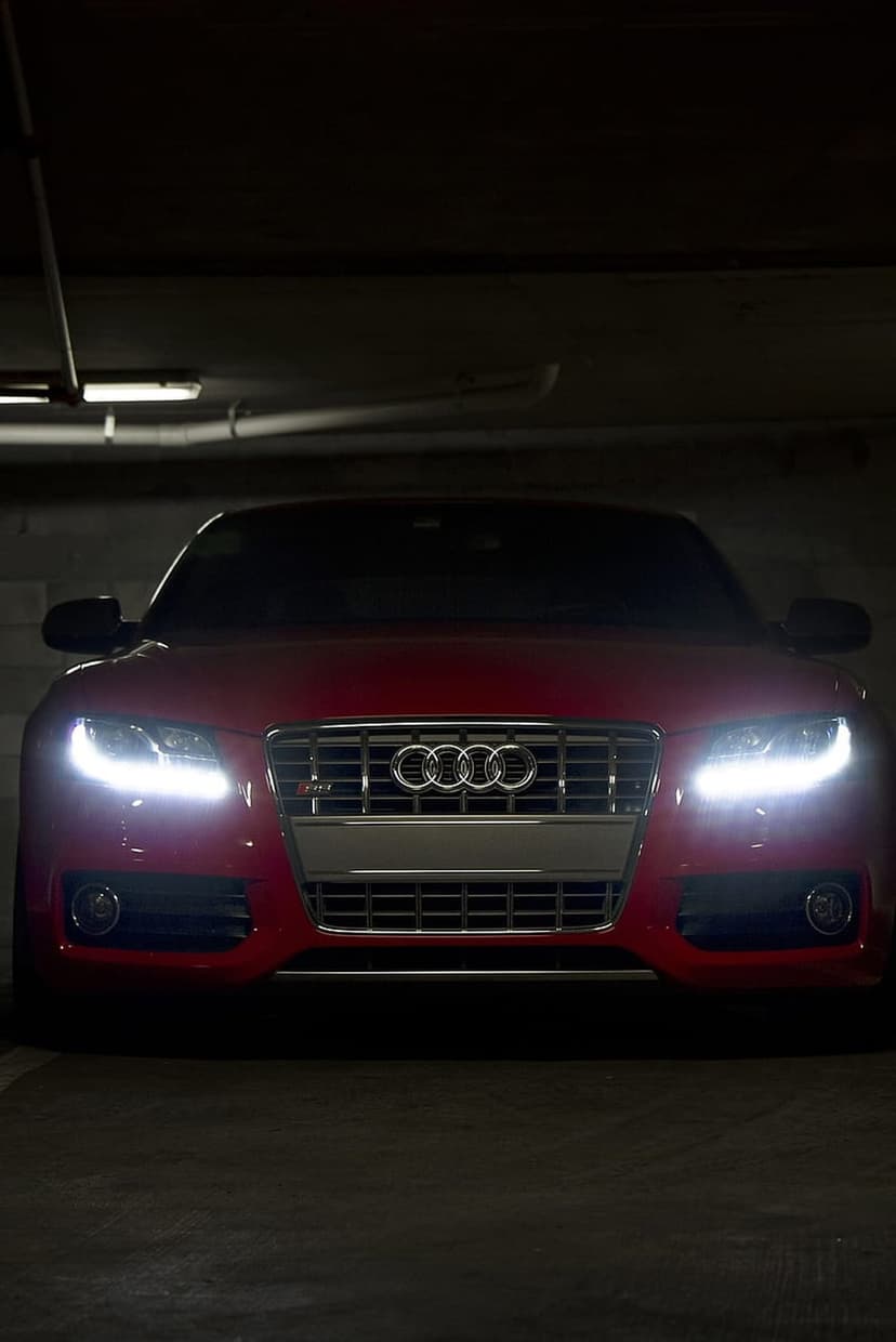 Red Audi RS5 with glowing headlights sits in a dark garage, highlighting the honeycomb grille and red paint.
