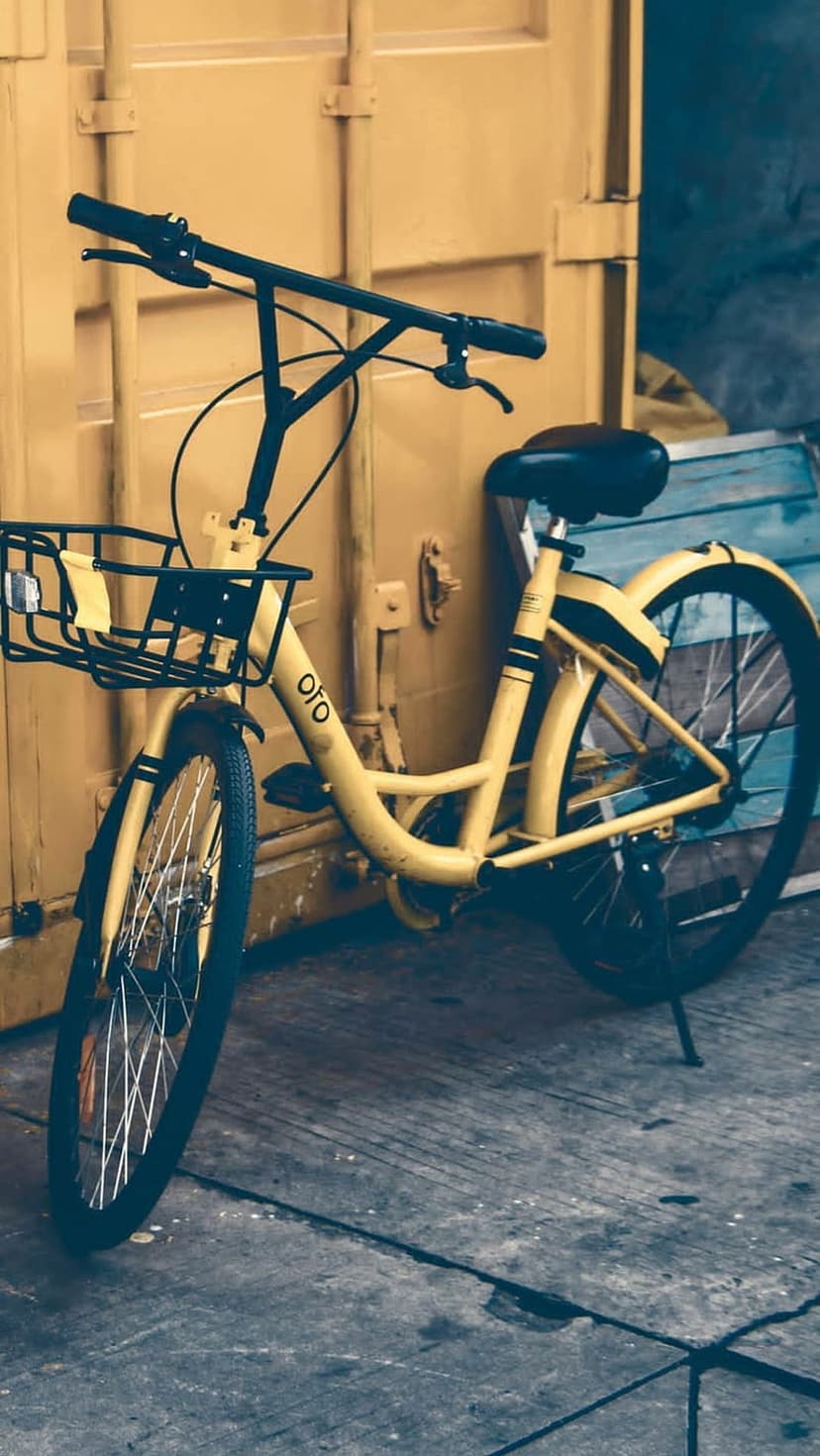 Yellow bicycle with a front basket parked against a weathered yellow shipping container on a concrete surface.