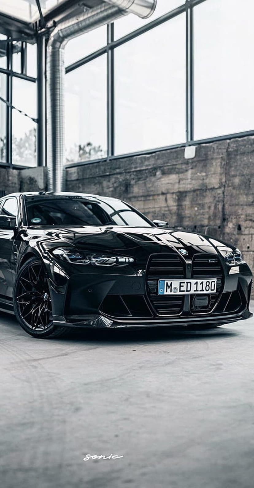 BMW M4 Coupe with illuminated headlights and a black finish parked inside a modern industrial garage space.