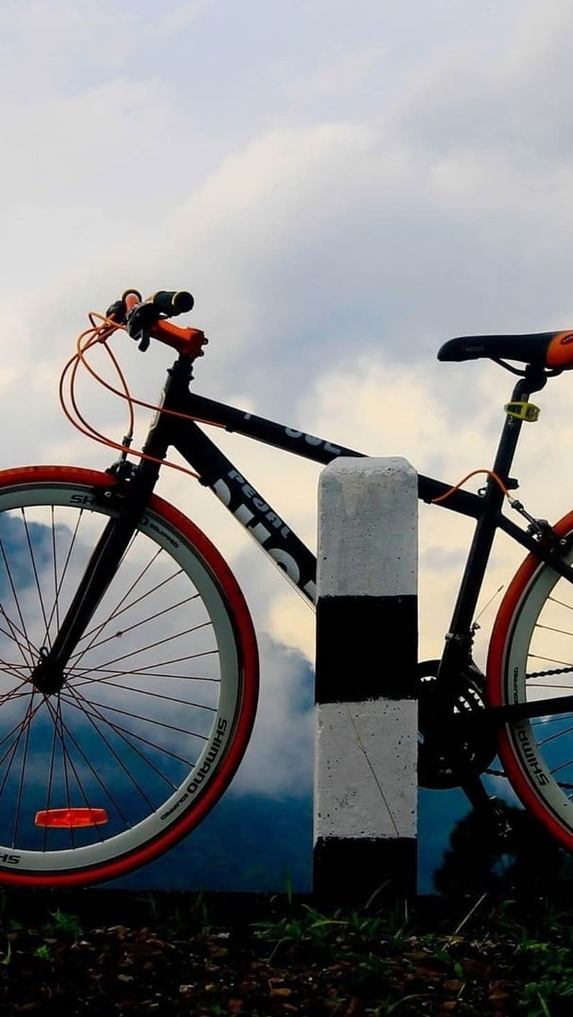 Black road bike with orange tires leaning on a striped pole against a backdrop of mountains and a cloudy sky.