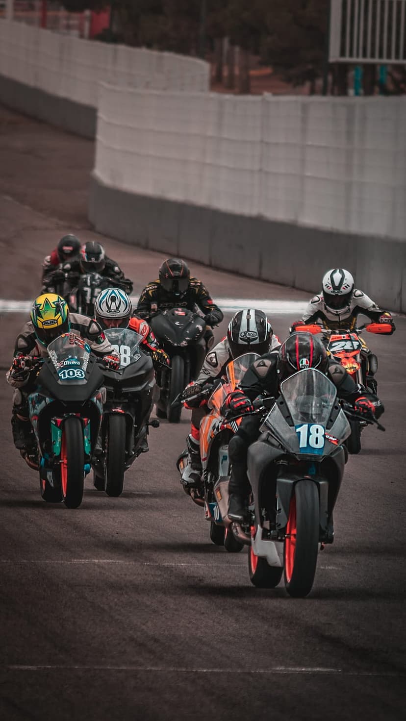 Professional superbike riders in colorful gear lean into a sharp asphalt curve on a competitive race circuit.
