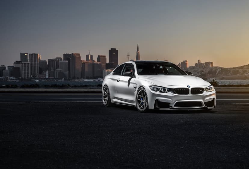 White BMW M4 coupe on a dark road with the San Francisco city skyline and Transamerica Pyramid at sunset.