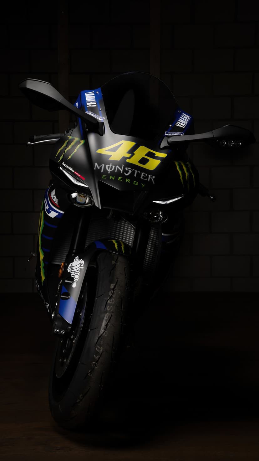 Valentino Rossi's Yamaha YZF-R1 motorcycle with Monster Energy decals parked against a dark textured brick wall.