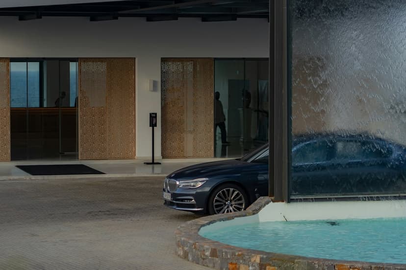 Dark blue BMW sedan parked at a luxury hotel entrance with a glass waterfall feature and wooden screen panels.