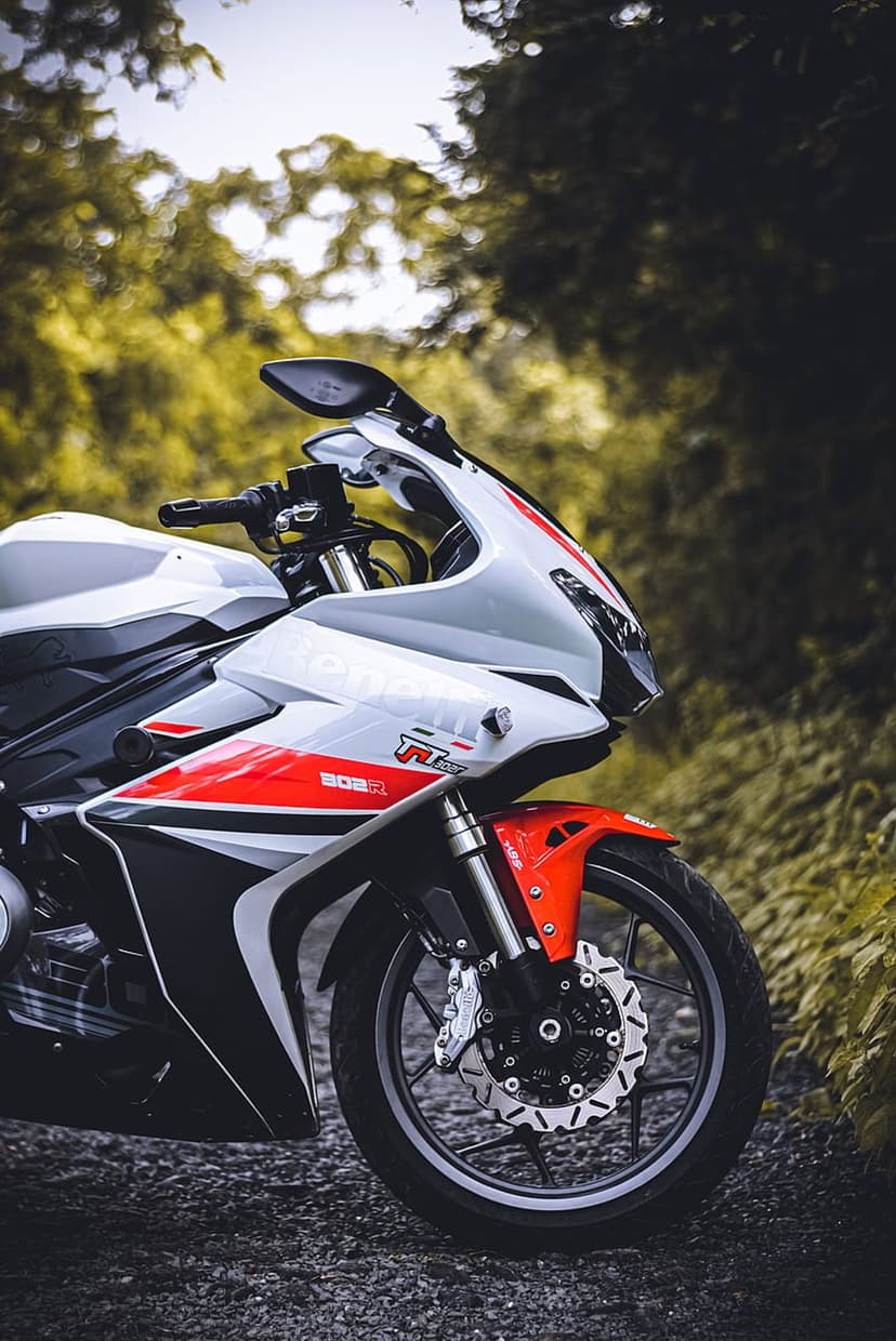 White and red sportbike motorcycle on a gravel road with lush green foliage and a blurred forest background.