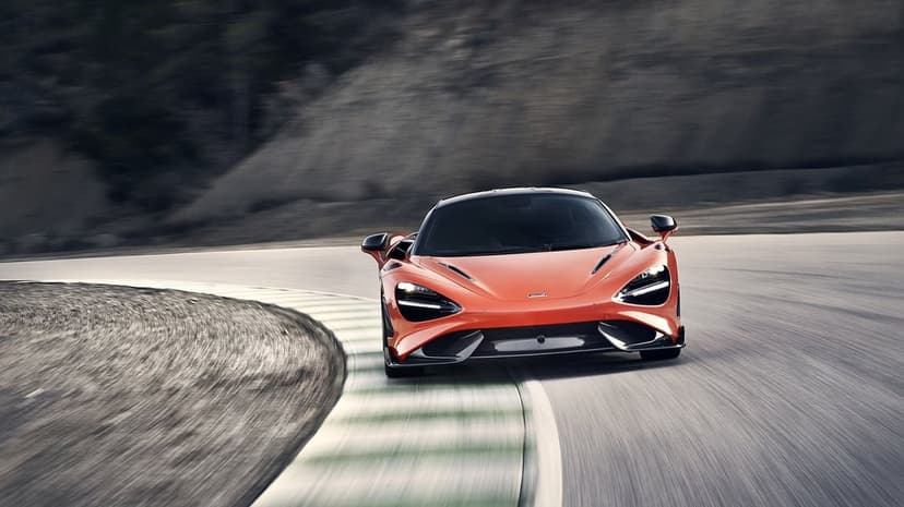 Orange McLaren supercar speeding through a race track curve with heavy motion blur and green rumble strips.