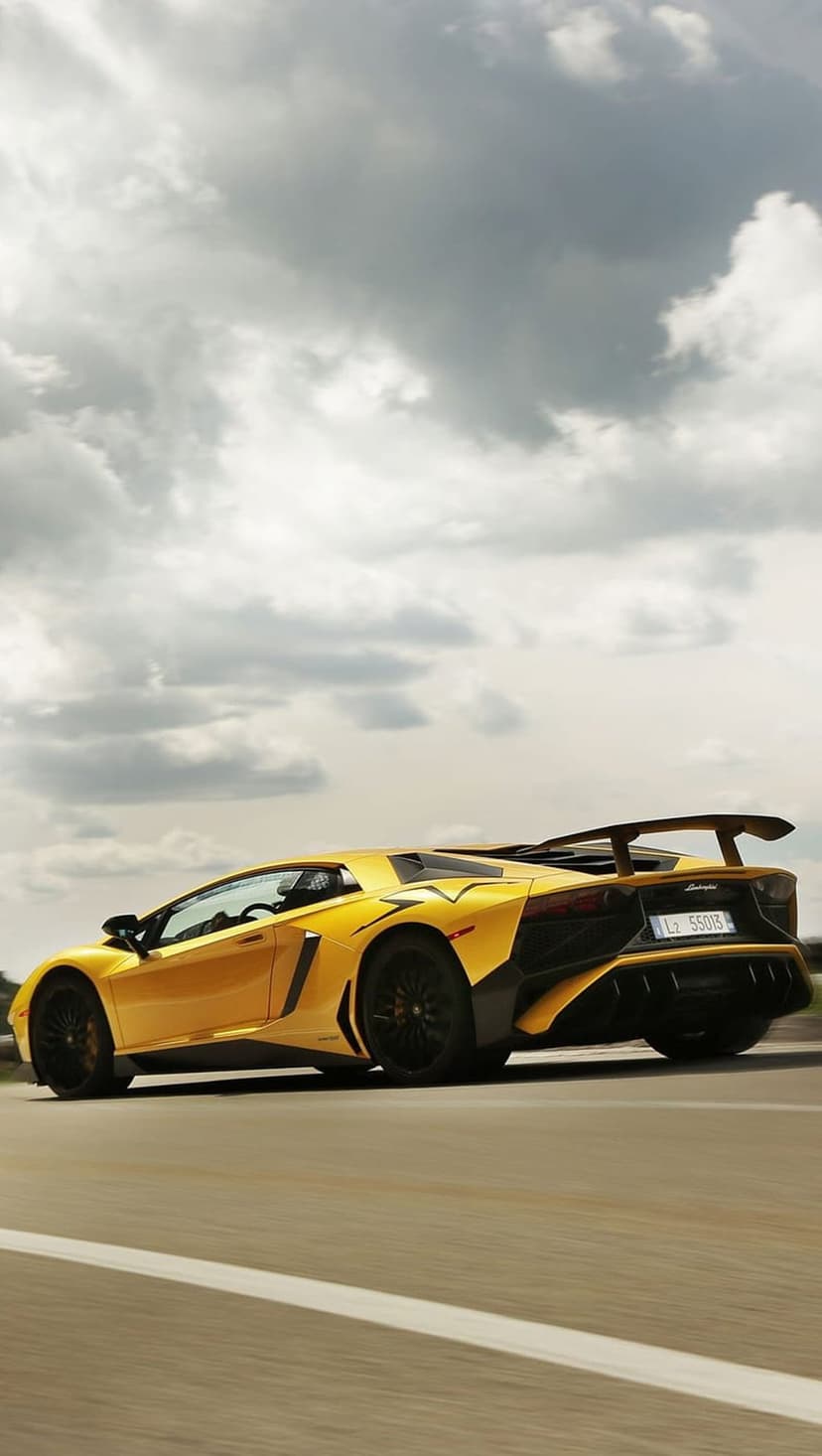 Yellow Lamborghini Aventador drives on a highway beneath textured grey clouds with its rear spoiler visible.