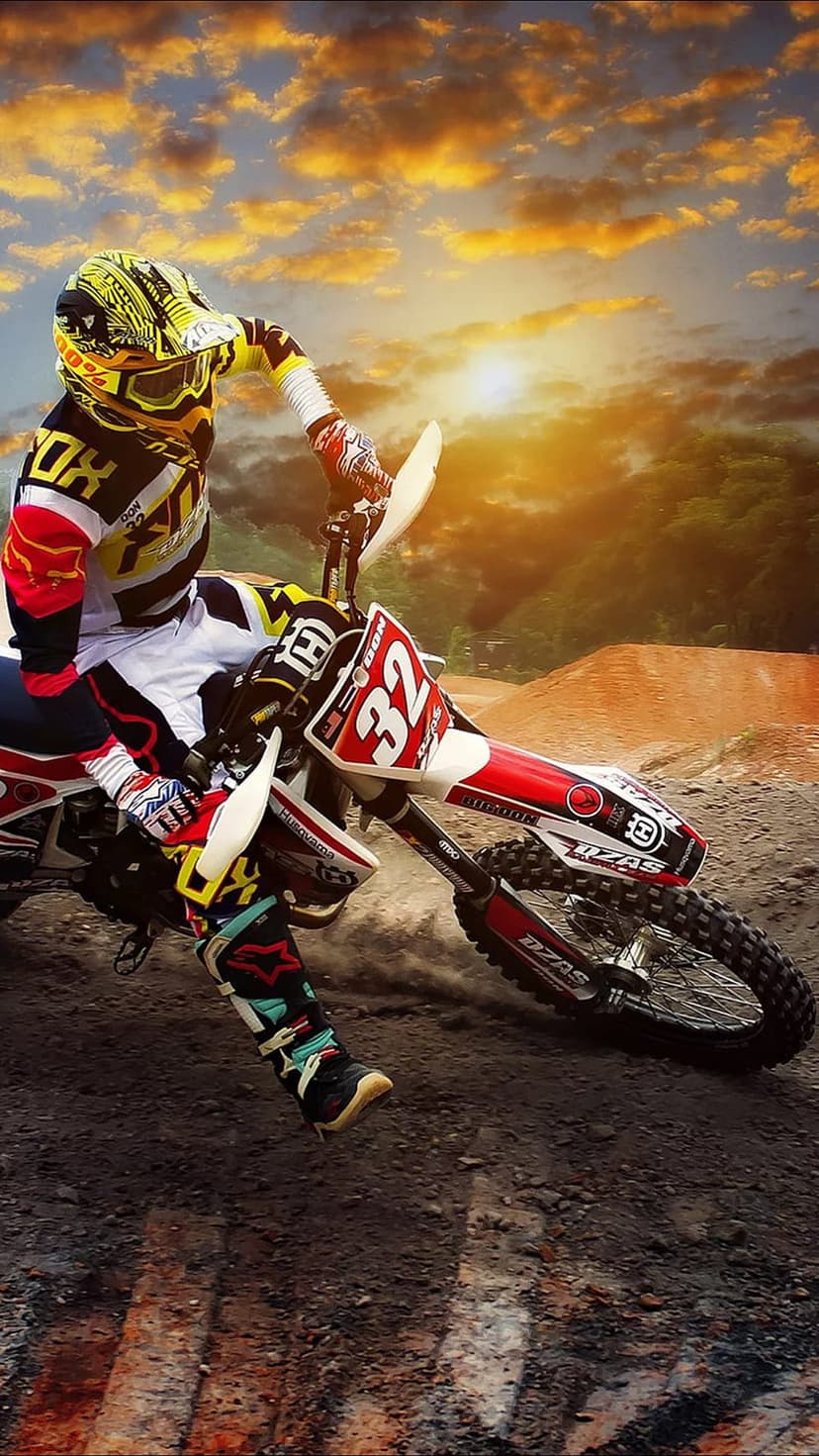 Motocross rider number 32 jumping mid-air on a dirt bike with a glowing sunset and clouds in the background.