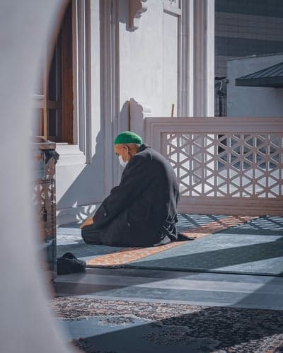 Man in green hat prays on prayer rug in mosque