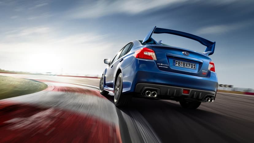 Blue Subaru WRX STI sports car drifting on a race track with motion blur and bright sunlight flare.