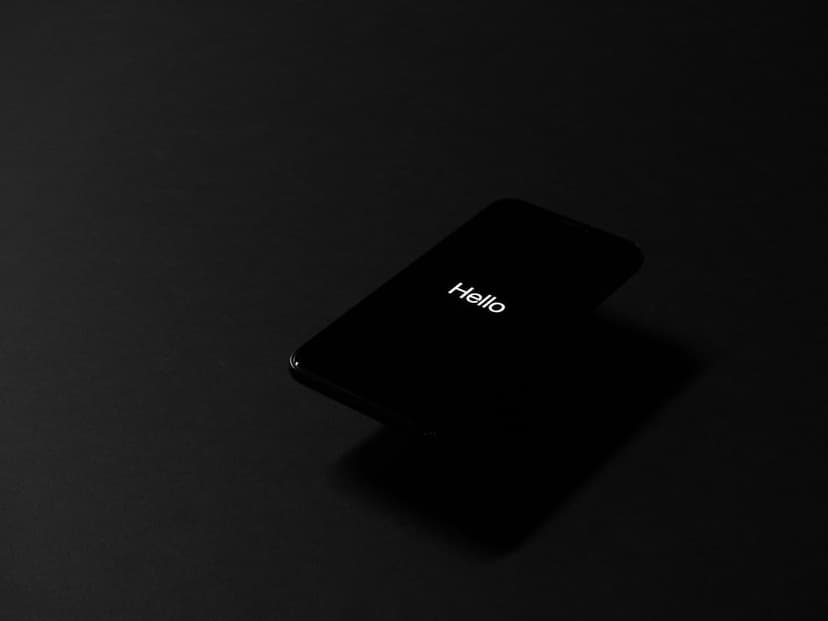 Black smartphone displaying white Hello text on its screen while resting on a dark surface with soft shadows.