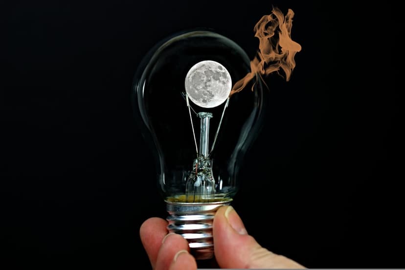 Lightbulb held by a hand features a glowing full moon inside with orange fire wisps emerging from the top.