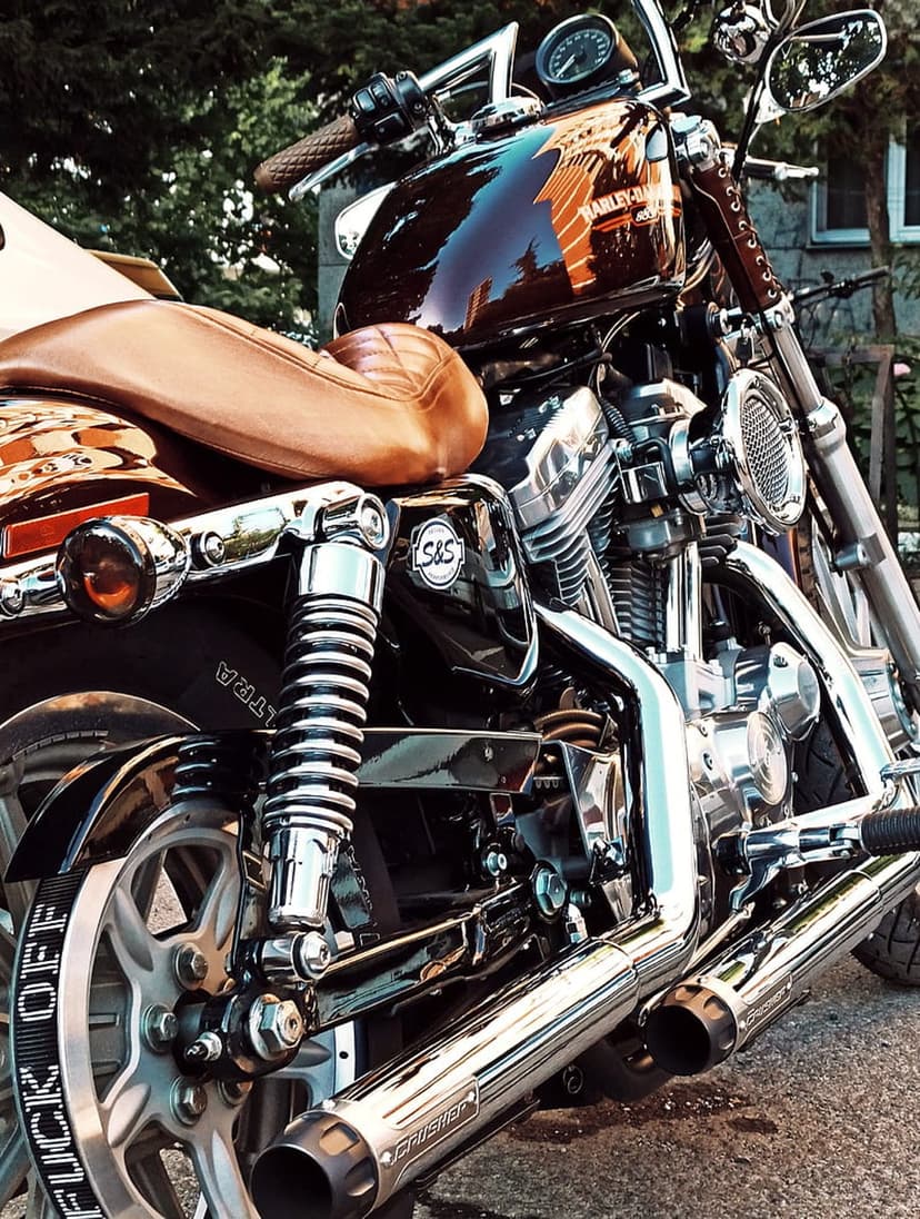 Polished Harley Davidson V-twin engine with chrome exhaust pipes and a textured brown leather motorcycle seat.
