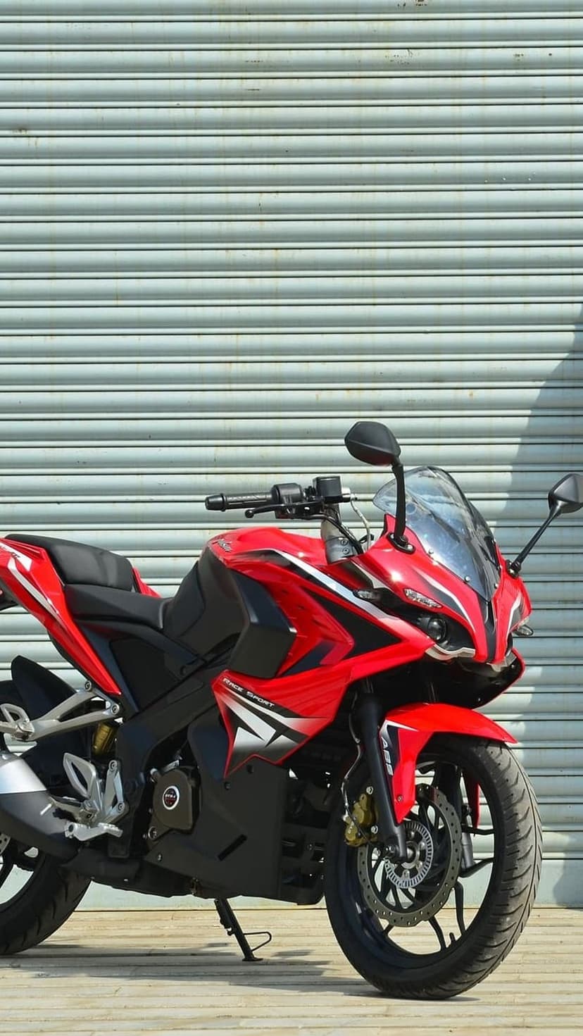 Red sport motorcycle with black accents parked against a gray corrugated metal door in a vertical urban setting.