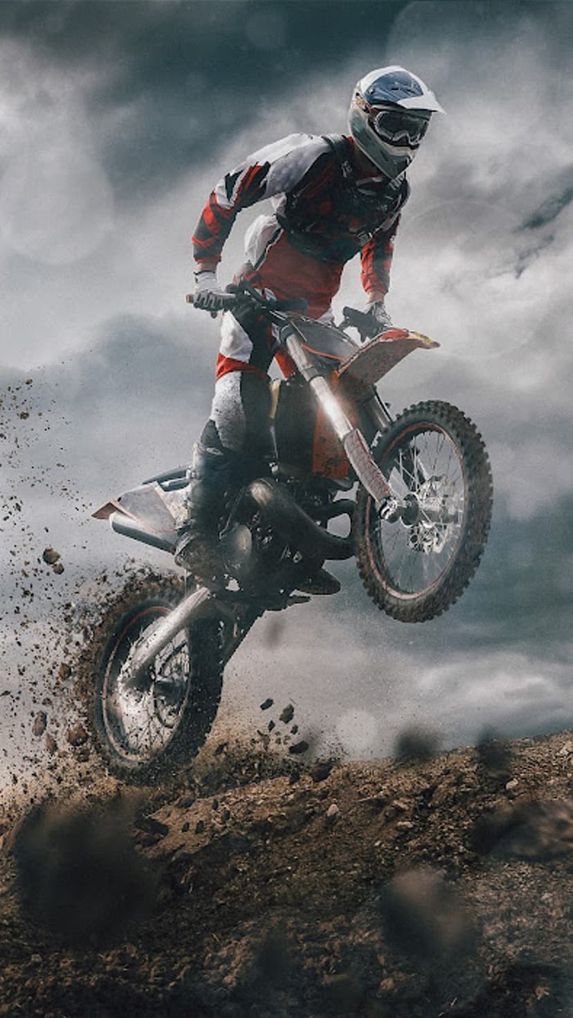 Motocross rider in mid-air above a dirt track with mud spraying from the bike against a cloudy, moody sky.