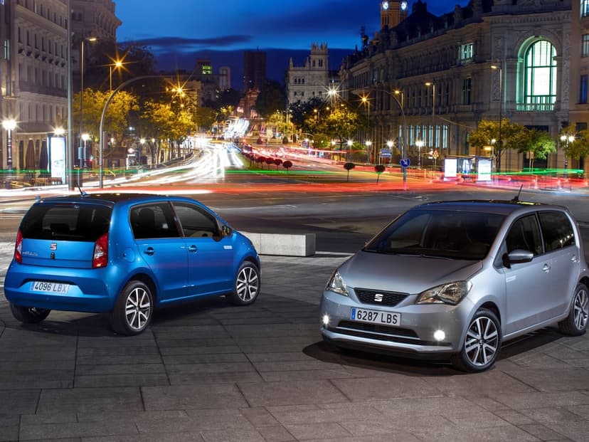 Blue and silver SEAT Mii Electric cars on a city plaza at night with long-exposure traffic light trails.