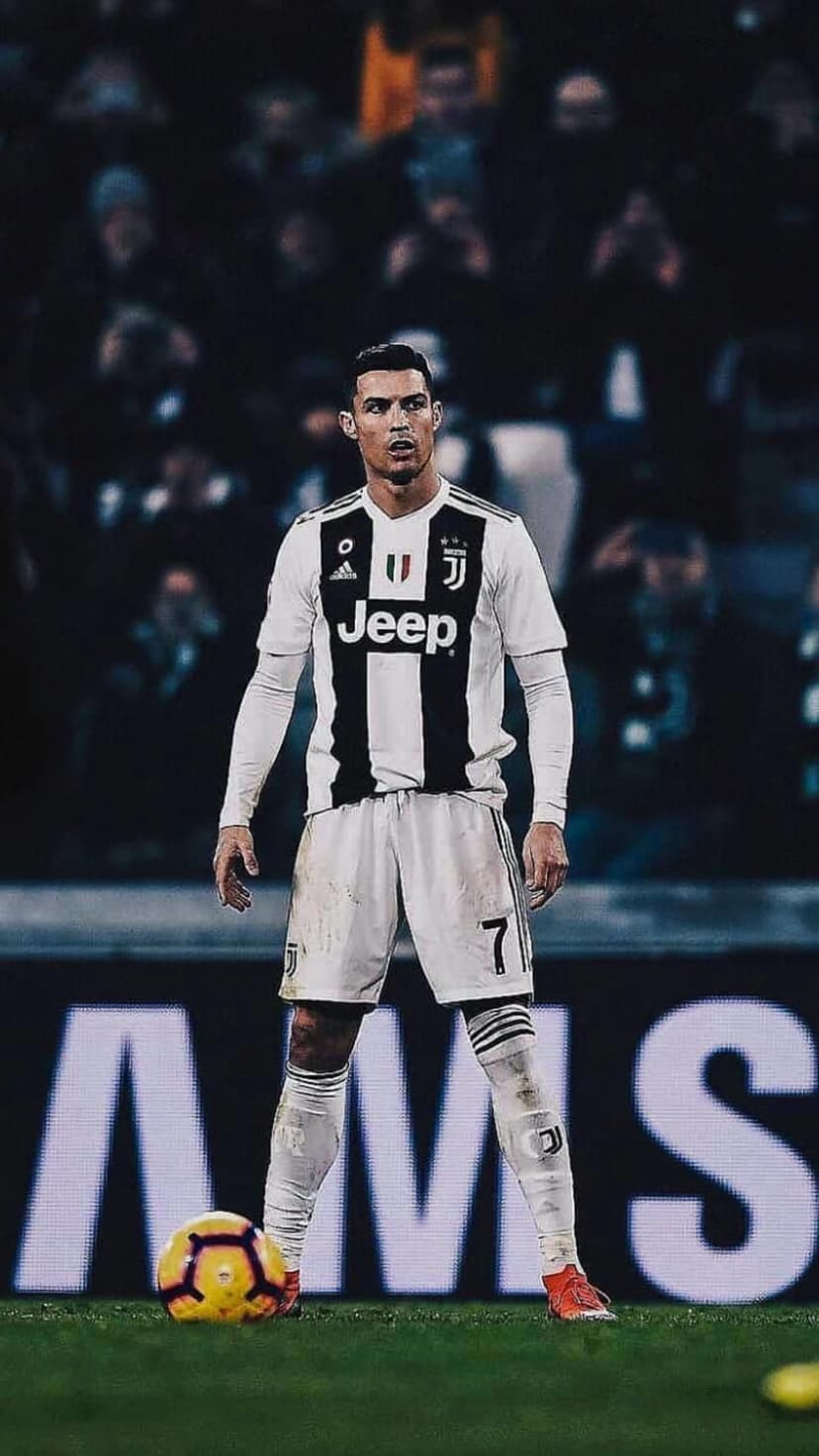 Cristiano Ronaldo stands in a black and white Juventus jersey holding a soccer ball inside a blurred stadium.