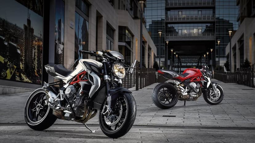 Silver and red MV Agusta Brutale motorcycles parked on a stone plaza between modern glass buildings at night.
