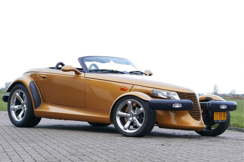 Gold Plymouth Prowler convertible with chrome wheels parked on a stone pavement against a neutral white sky.