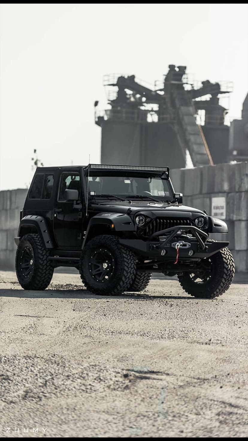 Black Jeep Wrangler with lifted suspension and aggressive tires parked in an industrial warehouse setting.