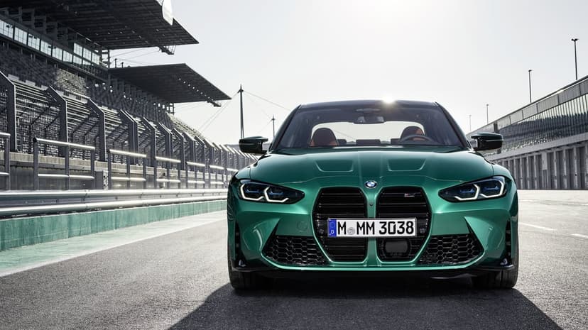 Green BMW M3 sports car parked on a racetrack with grandstands under bright sunlight in a front-view shot.