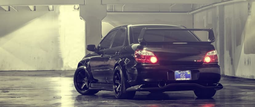 Rear view of a black widebody Subaru WRX STI in a concrete parking garage with glowing red taillights.