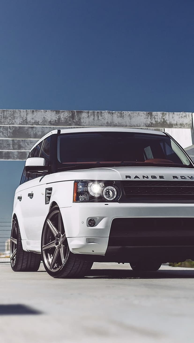 White Range Rover Sport SUV with custom wheels parked on concrete under a clear blue sky in vertical orientation.