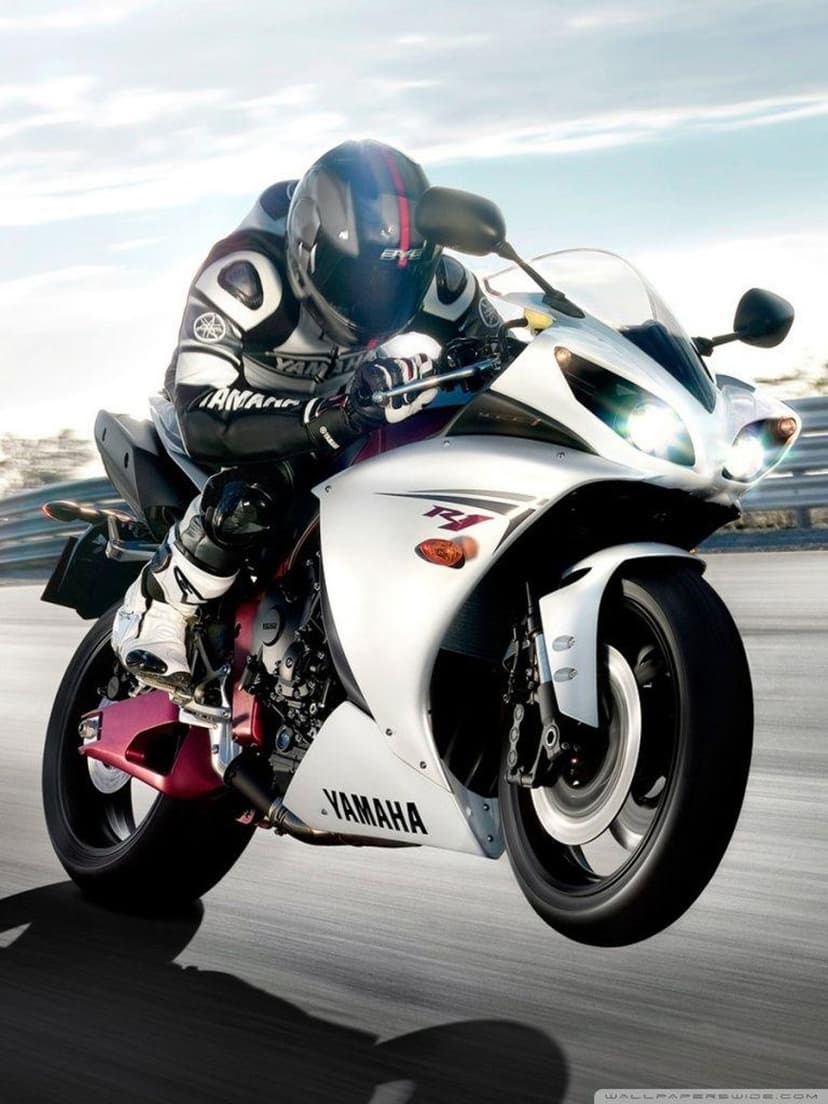 Yamaha R1 rider in red and white gear leans low into a racetrack curve during a high-speed motorcycle race.