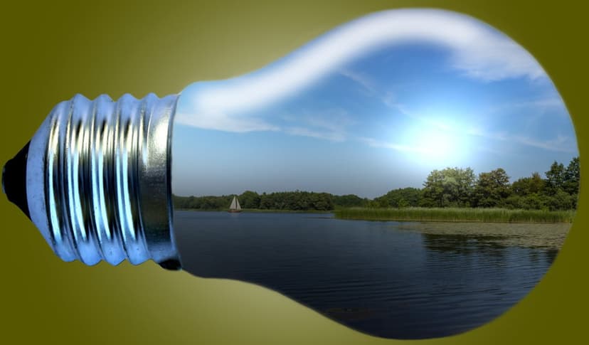 Lightbulb housing a miniature lake with a sailboat and green trees beneath a bright sun and blue sky.