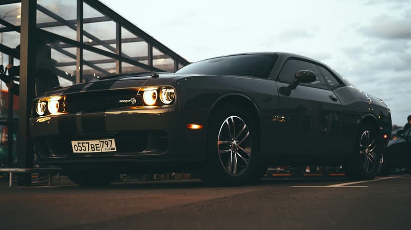 Dodge Challenger SRT Hellcat with lit headlights parked in a dark garage, shown from a low front angle.