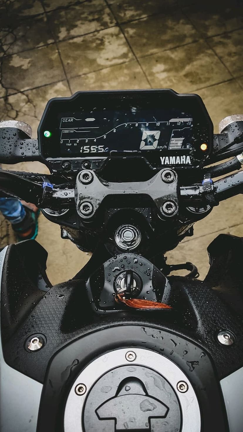 Yamaha motorcycle digital dashboard covered in raindrops with a key in the ignition and chrome fuel cap details.