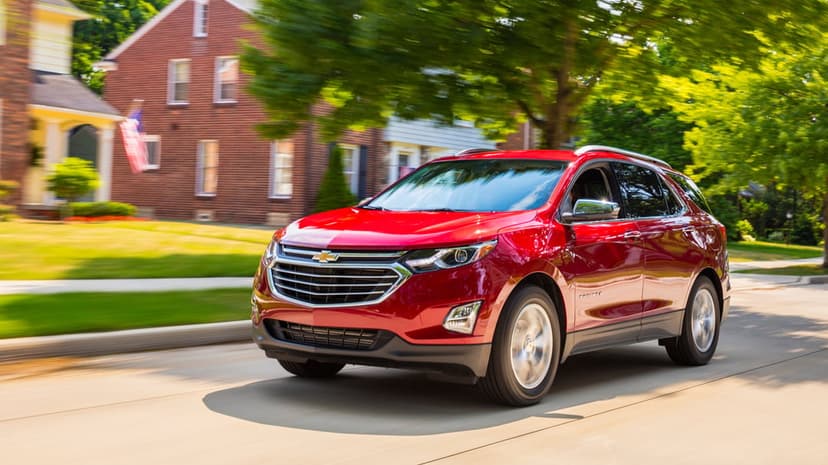 Red Chevrolet Equinox SUV driving on a sunny residential street with motion blur and green trees.