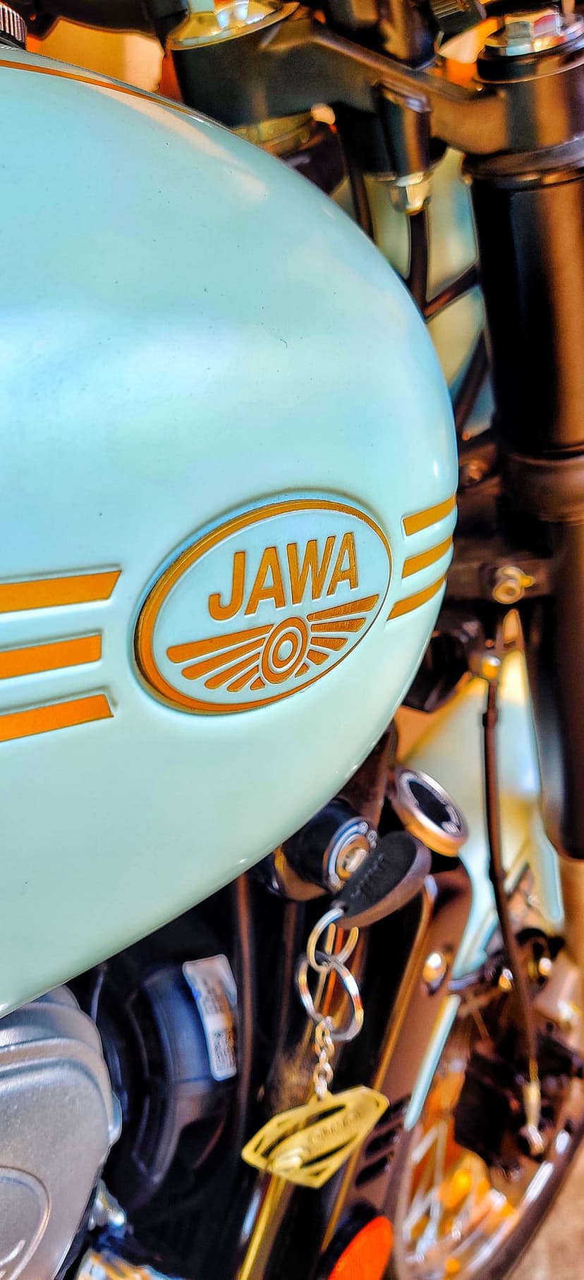 Jawa motorcycle logo with orange wings and a brass ignition key resting on a light blue metallic fuel tank.
