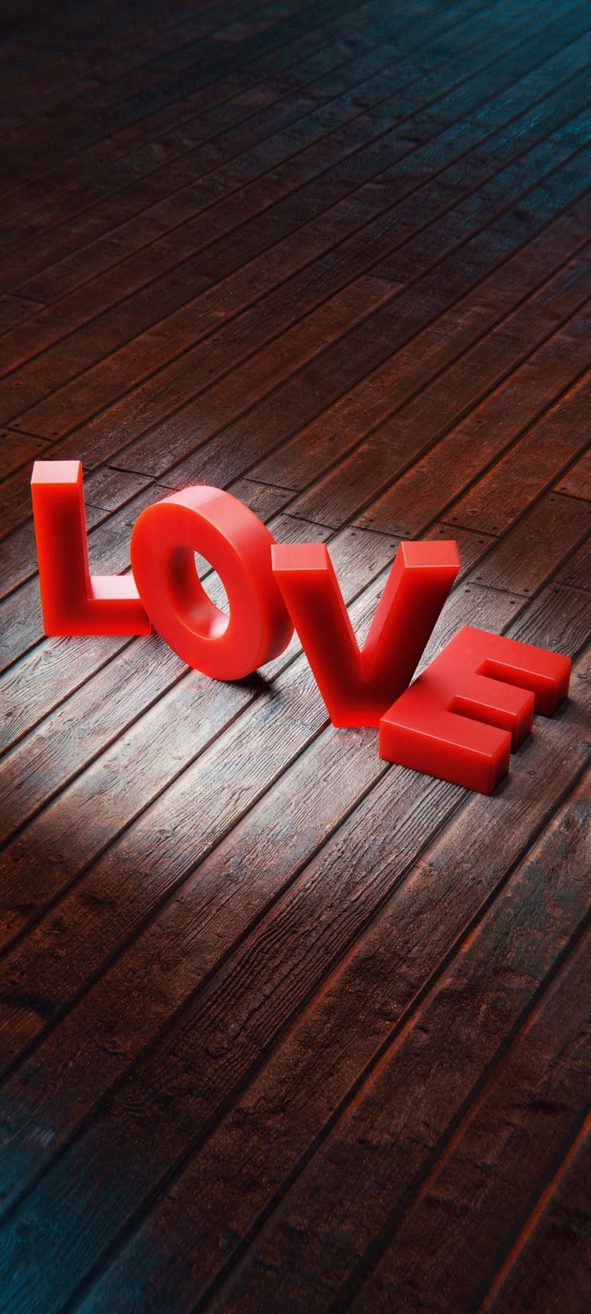 Red three-dimensional letters spelling LOVE sitting on a dark rustic wooden floor under soft glowing light.