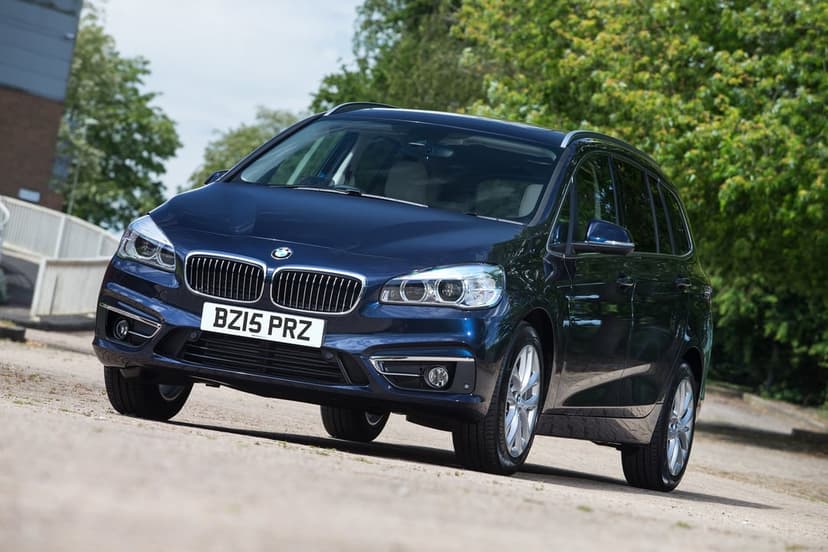 Dark blue BMW Gran Tourer parked on a paved road with green trees and soft daylight reflections.