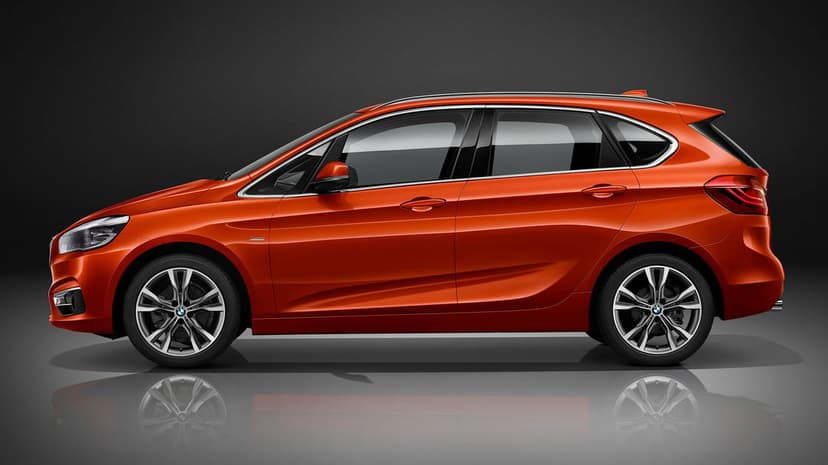 Metallic orange BMW 2 Series Active Tourer side profile on a dark reflective studio floor with soft lighting.