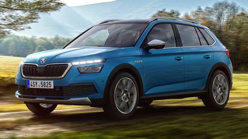 Blue Skoda Kamiq Scoutline SUV driving on a dirt road through a grassy field under a bright blue sky.
