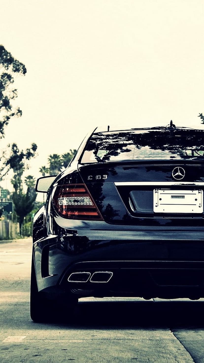 Mercedes-Benz C63 AMG rear view featuring quad exhaust pipes and red taillights on a palm-lined asphalt road.