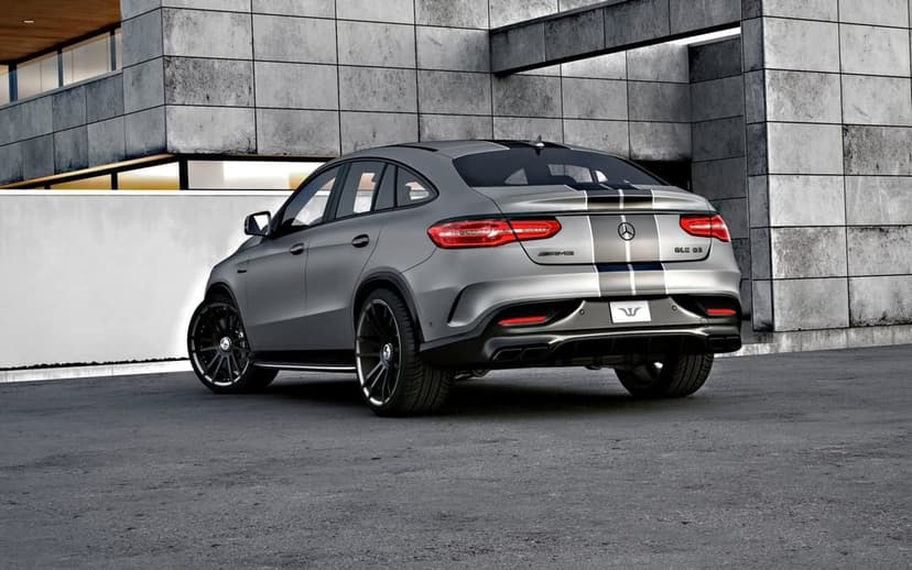 Matte grey Mercedes-AMG GLE 63 Coupe with racing stripes parked by a modern concrete building backdrop.