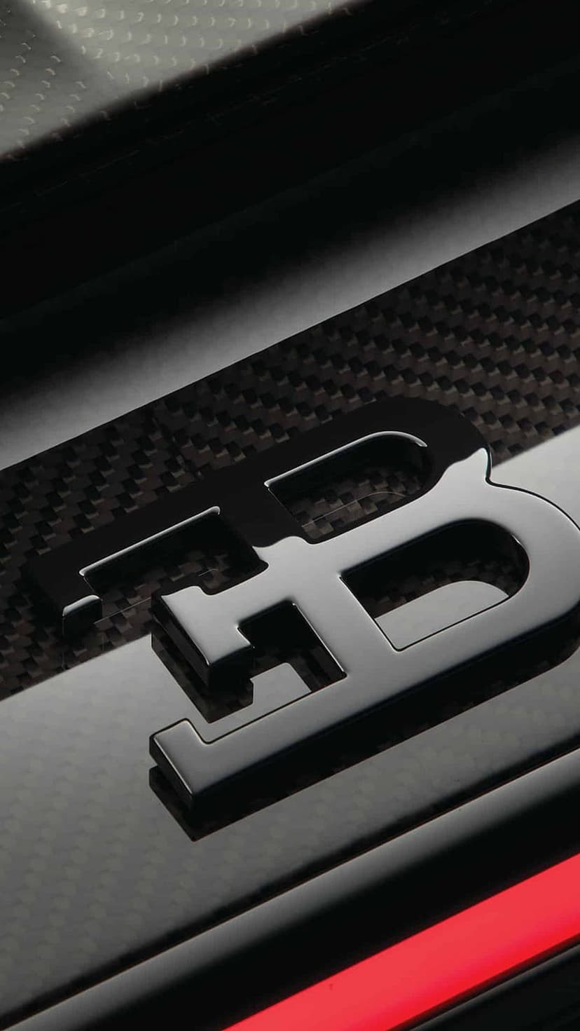 Bugatti EB logo in glossy black centered on textured grey carbon fiber with a thin horizontal red stripe below it.